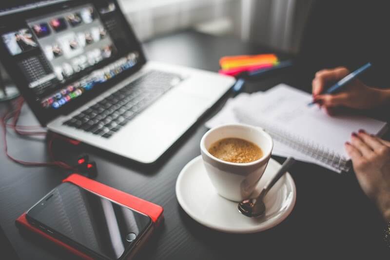 Video editor at video production company working and taking notes with cup of coffee